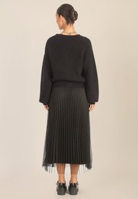 Czarny sweter z prążkowanej dzianiny z opadającymi ramionami, zestawiony z czarną plisowaną spódnicą midi. Strój ma tiulową warstwę na dole oraz masywne buty.