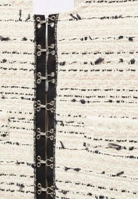 Agrafes noires attachées à des bandes de tissu noir sur un vêtement tissé texturé beige et noir.