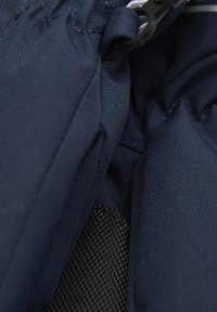 Nahaufnahme eines marineblauen Stoffes mit texturiertem schwarzen Patch und schwarzem Kunststoffclip an Outdoor- oder Sportgeräten.