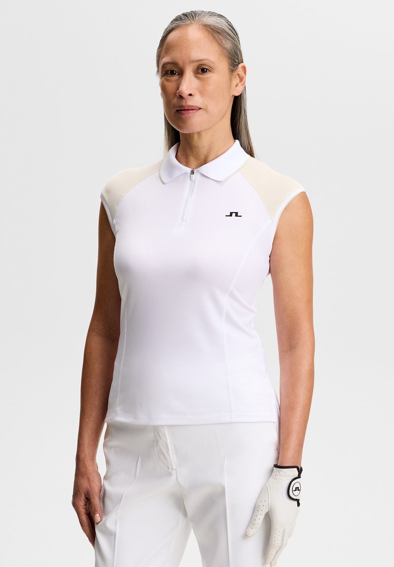 Polo blanc à manches courtes avec des accents beige clair, une fermeture éclair à l'avant et un logo noir brodé sur la poitrine. Porté avec un pantalon blanc et un gant de golf.