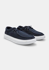 Tengerészeti vászon slip-on cipők lekerekített orral, fehér gumitalppal és tónusos fűzőkkel, a felső szélek mentén varrott részletezéssel.