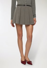 Donna che indossa una minigonna plissettata grigia con cintura nera e scarpe slingback borgogna a punta con fiocchi.