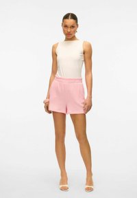 Lichtroze shorts met een gestructureerde weving, elastische taille, gecombineerd met een witte mouwloze top. Eenvoudig, strak ontwerp met zachte lijnen.