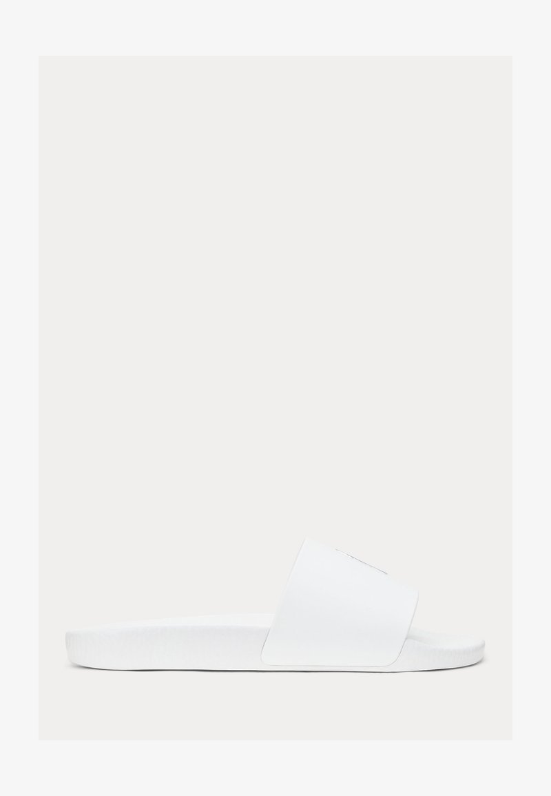 Sandalo con zeppa bianca con una larga fascia sopra il piede e una suola testurizzata, mostrato di profilo su uno sfondo neutro.