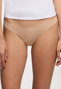 Perizoma beige realizzato in tessuto morbido ed elastico. Presenta un design minimalista e una fascia ampia in vita. Senza motivi visibili o accessori.