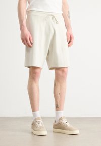 Bermudas texturizadas en tono beige claro con cintura ajustable, con rayas verticales. Combinadas con zapatillas beige y calcetines blancos hasta el tobillo.