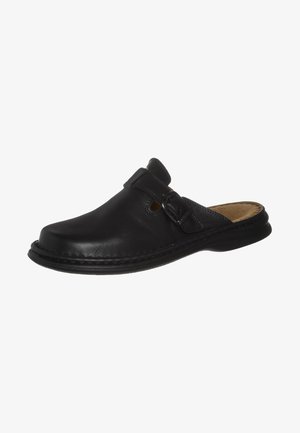 Black leather slip-on shoe with rounded toe, adjustable strap, textured side panel, and flat rubber sole.