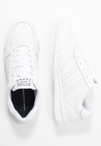 Weiße Sneakers mit einem oberen Teil aus glattem Leder, Schnürdesign, gepolsterter Zunge und Sohle. Merkmale beinhalten dezente Nähte und das Markenlogo auf der Zunge.