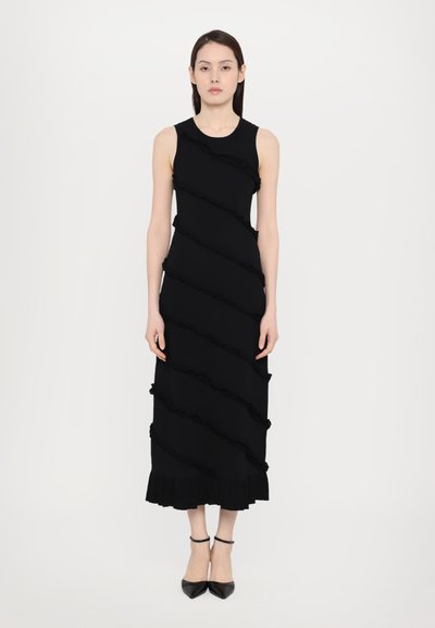 Black sleeveless dress featuring horizontal ruffled panels, a fitted silhouette, and a flared hem. Paired with black pointed-toe heels.