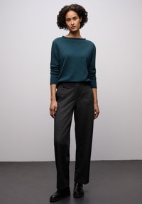 Miętowy sweter dziergany na drutach z długimi rękawami i dekoltem w łódkę, zestawiony z dopasowanymi, ciemnoszarymi spodniami. Całość dopełniają czarne botki.