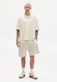 Beige sportoutfit met een losse mesh korte mouwen shirt en bijpassende shorts, vergezeld van een discreet logo. Sneakers en sokken inbegrepen.