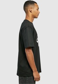 Sort bomulds T-shirt med korte ærmer og en afslappet pasform. Har et iøjnefaldende hvidt grafisk design på fronten, glat tekstur over det hele.