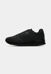 Zapatillas deportivas negras con parte superior texturizada, suela acolchada, materiales de tela y sintéticos, con un logo en el lado y cordones planos.