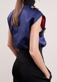 Navy satin topp med korta ärmar och en hög svart ribbad krage. Har dekorativa broscher och ett figursytt svart midjeband.