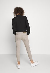 Beige cargo kalhoty s elegantním designem, elastickými manžetami na kotnících a čtyřmi kapsami. Nosené s černým volným tričkem a bílými teniskami.