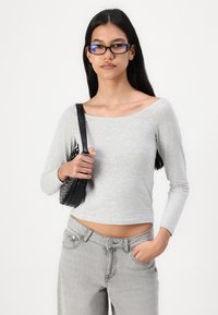 Svijetlosiva dugosleeve uska majica s otvorenim ramenima, uparena s visokim svijetlosivim trapericama i crnom torbicom preko ramena s okruglim zakovicama.