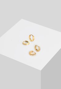 Quatre boucles d'oreilles en or en forme de créole avec des designs variés : deux simples, une texturée avec des rainures, et une ornée d'une rangée de petits cristaux transparents.