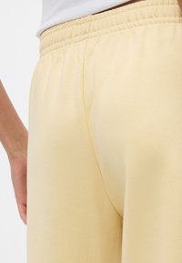 Κίτρινες, ελαστικές φόρμες με λάστιχο στη μέση, με απαλό ύφασμα και χαλαρή εφαρμογή, με  τις πλαϊνές ραφές ορατές από κοντινή γωνία.