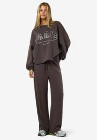 Ruskea huppari ja yhteensopivat verkkahousut, joissa on valkoinen "PARIS"-logo. Rento malli, pitkät hihat ja kevyt kangas. Tennarit täydentävät asun.