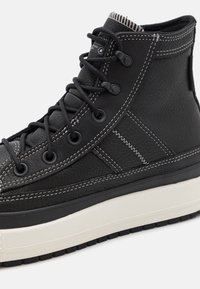 Black leather high-top sneaker with textured surface, contrasting white stitching, and a thick white rubber sole with textured black grip pattern.