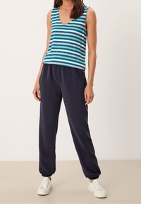 Haut sans manches rayé en sarcelle, bleu et blanc ; associé à un pantalon de jogging bleu marine avec des bordures élastiques. Design décontracté avec une coupe ample.