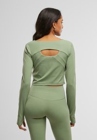 Világos zöld, hosszú ujjú crop top, hátul kivágással és testhez simuló szabással, sima anyagból, finom varrási részletekkel.