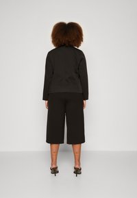 Chaqueta negra entallada de manga larga y corte recto, combinada con pantalones cortos de pierna ancha en negro. Llevado con sandalias de tacón negras.