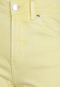 Jeans de ganga amarelos com um design clássico de cinco bolsos, fecho de botão metálico e costura em contraste para um detalhe adicional.