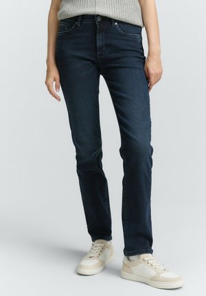Donkerblauwe spijkerbroek met een slim fit, voorzien van vijf zakken, een knoop- en ritssluiting, en lichte vervaging. G gedragen met beige sneakers.