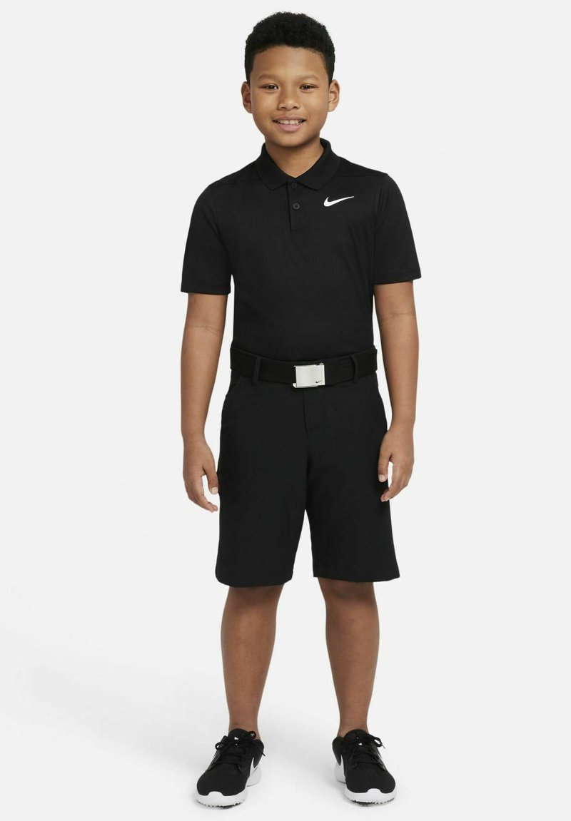 Svart polo skjorta med krage och vitt Nike-logotyp, kombinerad med svarta shorts och ett svart bälte med silverfäste. Svarta sneakers.