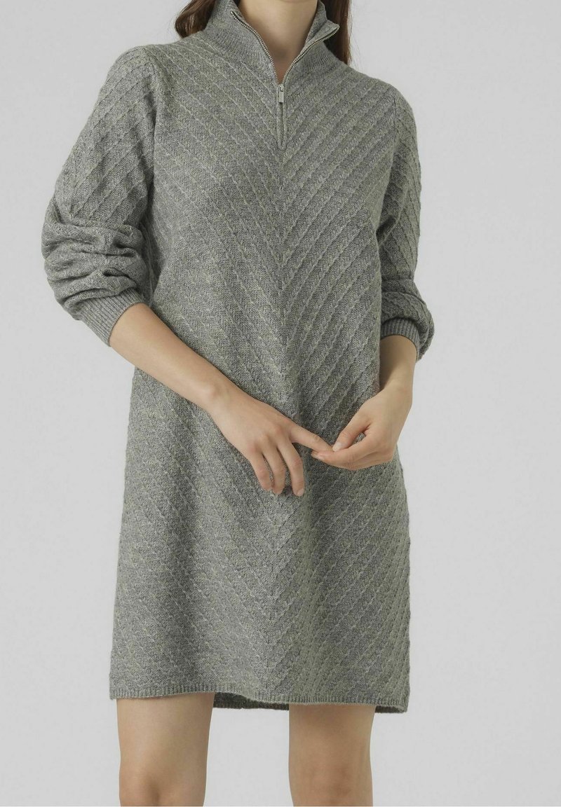 Robe tricotée grise avec un col à fermeture éclair à moitié, présentant un motif chevron texturé et des manches amples, arrivant à mi-cuisse.