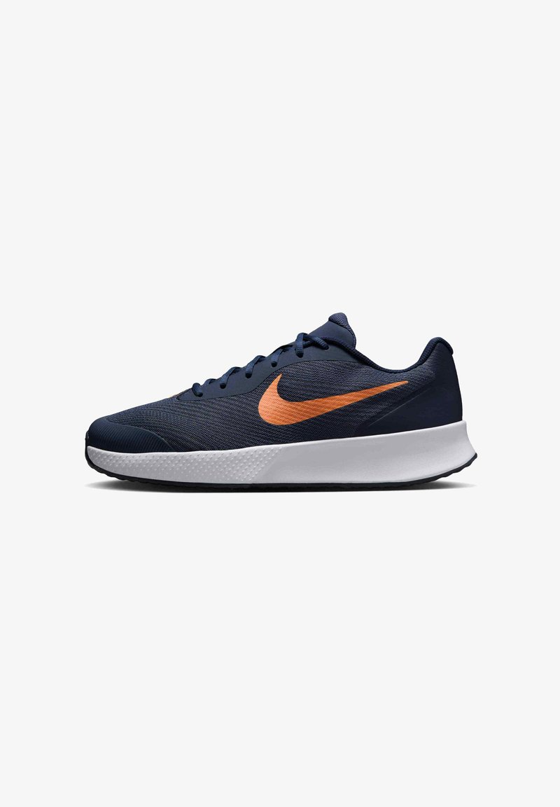Tumed sinine spordijalanõud, millel on oranž Nike'i lõikejoon, kergest võrgust pealispind, pehmendatud krae ja valge vahe- ning tekstureeritud must välispind.