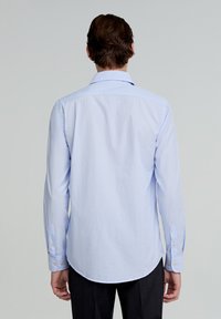 Chemise à manches longues rayée bleu clair, avec poignets à boutons, ourlet arrondi, tissu lisse, couture visible le long des coutures.
