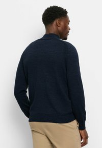 Marineblauer Pullover mit strukturiertem Strick, geripptem Saum und langen Ärmeln. Verfügt über einen Stehkragen und dezente Nahtdetails an den Schultern.