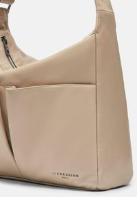 Beżowa skórzana torebka o luźnym fasonie, z zamykaną kieszenią i zewnętrzną kieszenią wsuwaną, oznaczona logo "LIEBESKIND BERLIN".