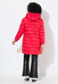 Röd puffjacka med huva, har kvarterat mönster och elastiska ärmslut. Matchas med glänsande svarta utsvängda byxor och silverstövlar.