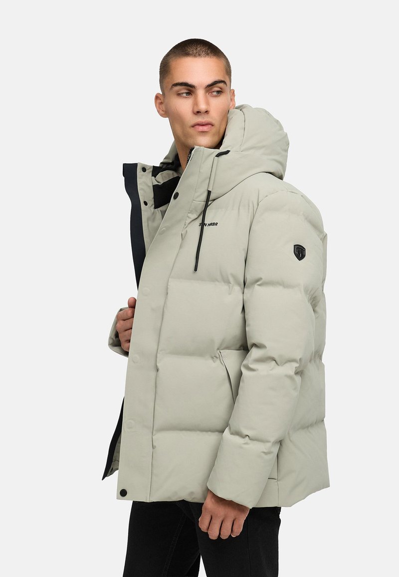 Šviesiai pilkas pūkinis švarkas su kapišonu, turintis užtrauktuką, juodus akcentus ir emblema ant rankovės. Textūruota, šilumą izoliuojanti medžiaga.