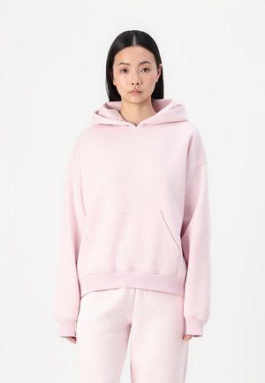 Light pink hoodie made of soft fabric, featuring a front pocket, ribbed cuffs, and a drawstring hood. Paired with matching sweatpants.