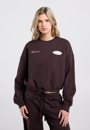 Bruine cropped trui van dikke stof met lange mouwen. Voorzien van witte tekst "RESET MODE" en een roze ovaal logo aan de voorkant.