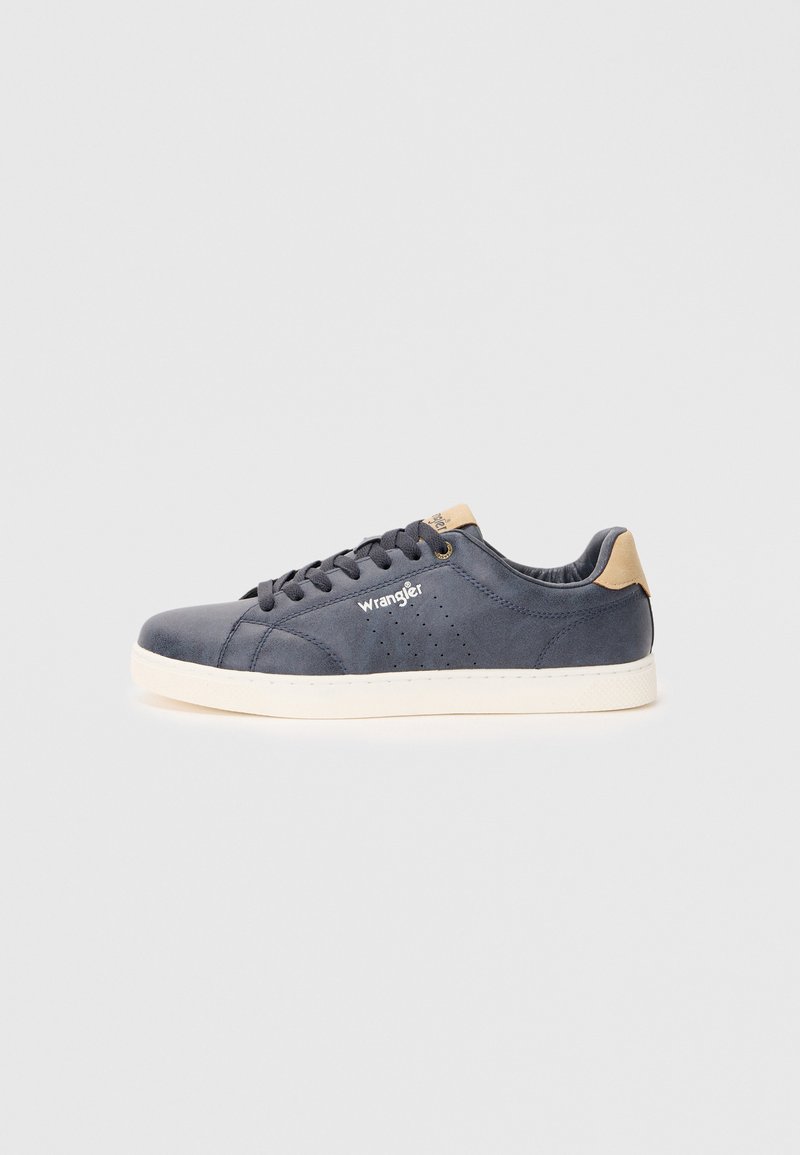 Baskets en cuir bleu marine avec des perforations, semelle en caoutchouc blanche, accent de talon marron et logo "Wrangler" sur le côté.