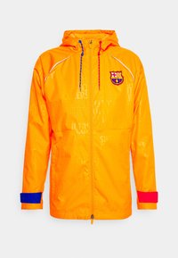 Ljus orange vindtät jacka med vita detaljer, FC Barcelona-logga, justerbara röda och blå snören samt kontrasterande ärmmuddar i blått och rött.
