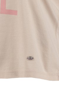T-shirt en coton couleur crème avec un design en lettres roses et une étiquette emblématique argentée portant l'inscription "MY LARGO" près de l'ourlet. Texture lisse.