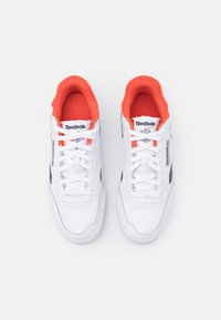 Paire de baskets blanches Reebok Classic avec des accents noirs et une doublure intérieure orange vif, vues de dessus sur un fond blanc.