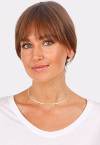 Guldfarvet metal choker halskæde, glat tekstur, cirkulært design, minimalistisk stil. Båret med en hvid V-hals t-shirt, der viser et simpelt look.