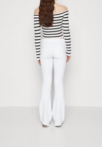 Haut court à rayures dénudant les épaules en noir et blanc, associé à un pantalon évasé blanc ajusté. Textures lisses avec un minimum de détails.