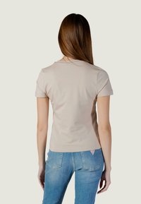 Camiseta de manga corta color beige claro con cuello redondeado, textura suave y diseño ajustado, combinada con vaqueros de mezclilla azul claro que llevan una etiqueta.