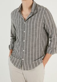 Grijs gestreefd overhemd met witte verticale strepen, met een klassieke kraag en opgerolde mouwen, gemaakt van textuurstof.