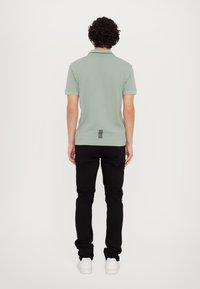 Light green polo shirt with short sleeves, featuring a black accent pattern at the back, paired with black pants and white sneakers.