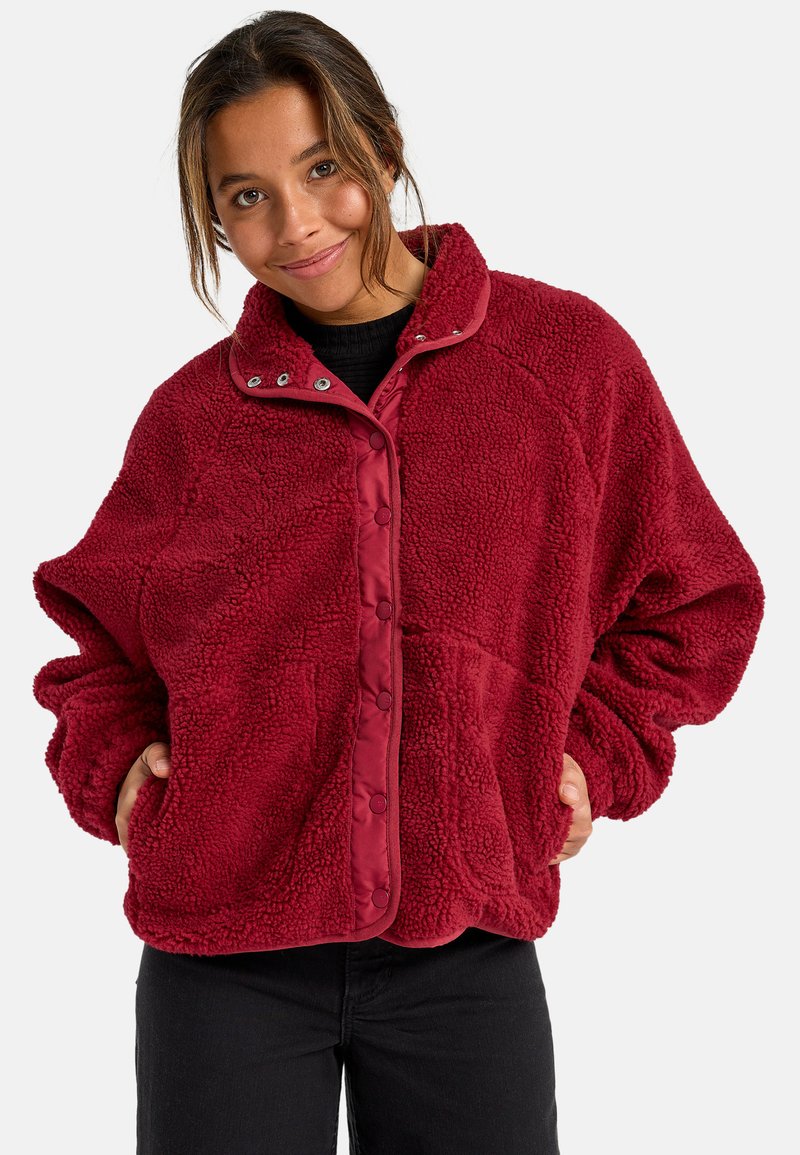 Giacca in pile rossa con superficie testurizzata, bottoni a scatto e colletto a contrasto. Presenta tasche laterali e una vestibilità rilassata.