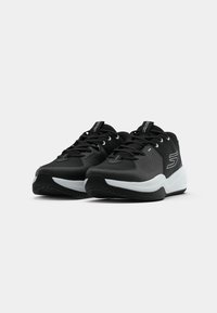 Des chaussures de sport noires avec une texture lisse, des panneaux en maille et une semelle intermédiaire blanche, ornées de lacets noirs contrastants et d'un logo sur le côté.